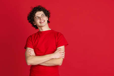 Cropped portrait of young man in casual cloth smiling and looking away isolated over red backgroundの写真素材