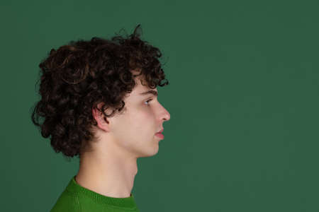 Cropped side view portrait of young man in green sweater looking away isolated over dark green backgroundの写真素材