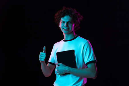 Cropped portrait of young man in white T-shirt with tablet showing like gesture isolated over black...