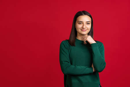 Cropped portrait of young beautiful smiling woman in green sweater isolated over red background