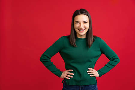 Cropped portrait of young beautiful woman in green sweater expressively smiling isolated over red backgroundの写真素材