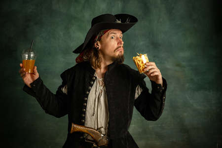 Portrait of one brutal man, medeival pirate holding orange juice and fries isolated over dark background.の写真素材