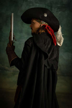 Cropped portrait of brutal frightening man, medeival pirate in vintage costume with sword and gun...