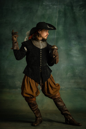Portrait of brutal horrendous man, medeival pirate in vintage costume holding sword isolated over dark background. Swordcraftの写真素材