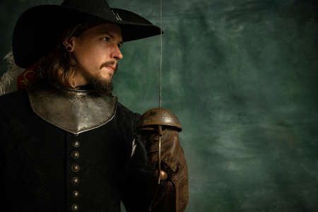 Portrait of brutal horrendous man, medeival pirate in vintage costume holding sword isolated over...