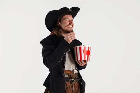 Cropped portrait of brutal smiling man, pirate in vintage costume eating popcorn isolated over white backgroundの写真素材