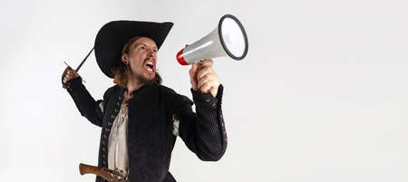 Cropped portrait of man, pirate in vintage costume raising sword and shouting in megaphone isolated...