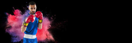 Creative collage of young man, professional boxer training isolated over colorful powder explosion on black background. Flyerの写真素材