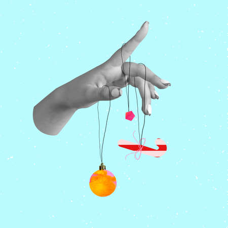 Contemporary art collage of female hand holding Christmas tree toys, decorations isolated over blue backgroundの写真素材