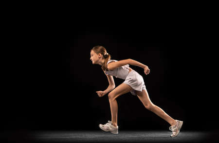 Full-length portrait of teen girl, athlete running, training isolated over black background