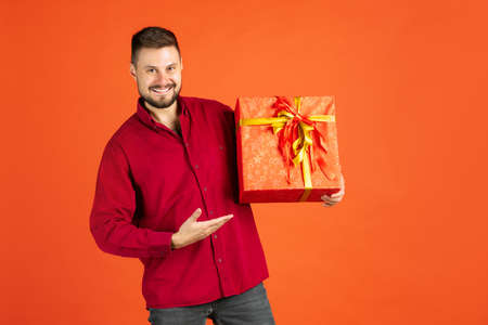 Cropped portrait of man in shirt holding gift box cheerfully posing isolated over red backgroundの写真素材