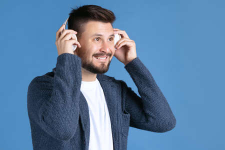 Cropped portrait of happy man listening to music in white headphones isolated over blue background