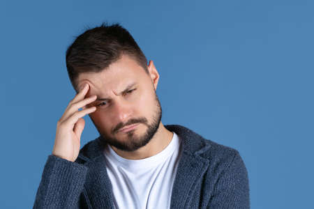Cropped portrait of seriously looking, tired man touching head, thinking isolated over blue...