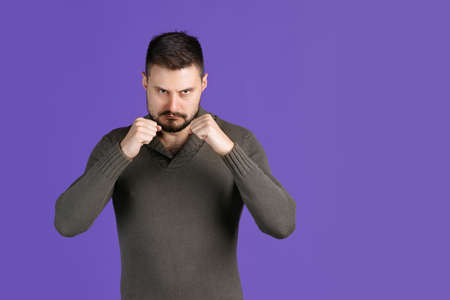 Cropped portrait of seriously looking man raising fists like boxer, posing isolated over purple...