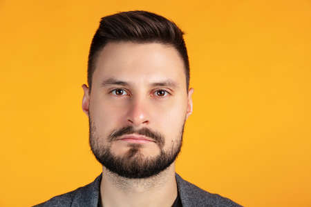Close-up portrait of serious man looking at camera, posing isolated over yellow backgroundの写真素材