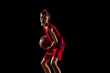 Cropped portrait of boy, basketball player in special uniform training isolated over black backgroundの写真素材