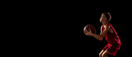 Cropped portrait of concentrated basketball player in uniform throwing ball into the basket isolated over black background. Flyerの写真素材