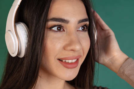 Close-up portrait of beautiful young woman, girl in white headphones isolated over green backgroundの写真素材
