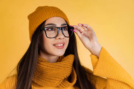 Cropped portrait of young beautiful girl in glasses attractively looking away isolated over yellow backgroundの写真素材