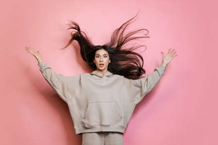 Cropped portrait of young beautiful girl posing isolated over pink background. Hair flipの写真素材