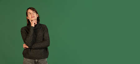 Cropped portrait of beautiful woman with thoughtful, dreaming expression posing isolated over green backgroundの写真素材