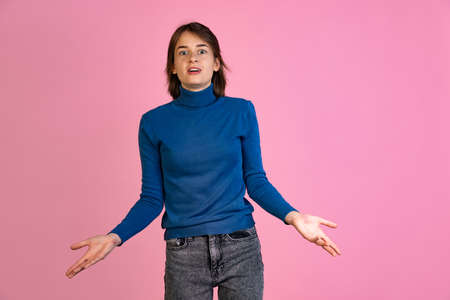 Cropped portrait of young woman spreading hands in misunderstood expression isolated over pink backgroundの写真素材