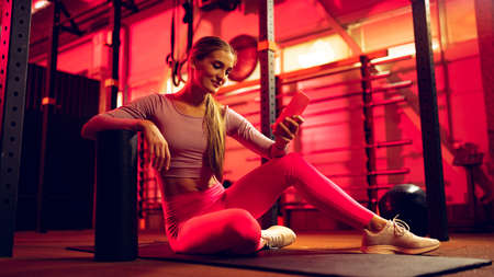 Full-length portrait of young sportive girl in pink sportswear training online in gym. Online fitness trainerの写真素材