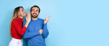 Cropped portrait of happy couple, woman whispering to exciting man gossips, news isolated over blue background. Flyerの写真素材