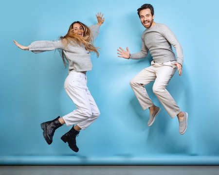 Portrait of young cheerful couple, man and woman, and jumping together isolated over blue backgroudの写真素材