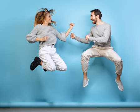 Full-length portrait of young cheerful couple jumping and jokingly fighting together isolated over blue backgroudの写真素材