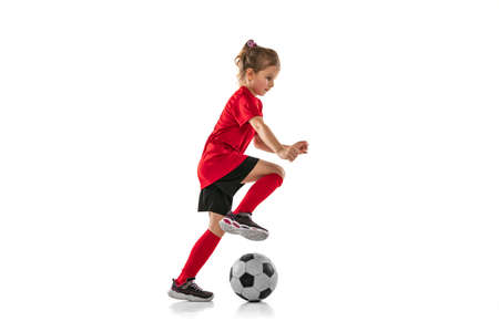 Full-lenght portrait of little sportive girl in red uniform playing team game, training football...