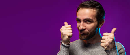 Portrait of man showing like gesture in excitement, posing isolated over purple background in neon lights. Flyerの写真素材