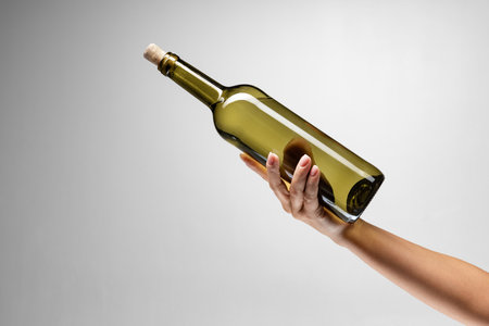 Cropped image of female hand holding bottle of delicious wine isolated over gray backgroundの写真素材