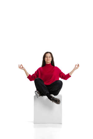 Full-length portrait of young calm girl sitting in lotus yoga pose isolated over white backgroundの写真素材