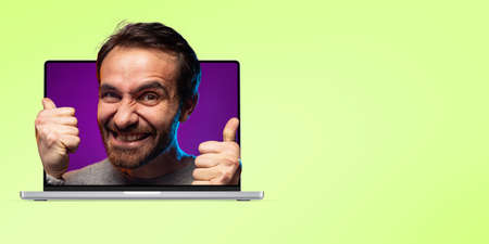 Creative collage. Excited man sticking out laptop screen isolated over green background
