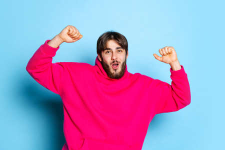 Cropped studio portrait of young excited boy holding fists up isolated over blue backgroundの写真素材