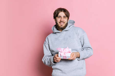Cropped portrait of smiling young man holding present box isolated over pink studio background