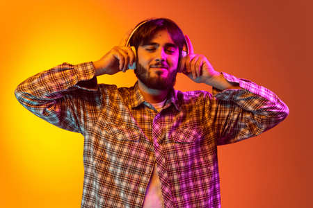 Cropped portrait of young boy in checkered shirt listening to music in headphones isolated over...