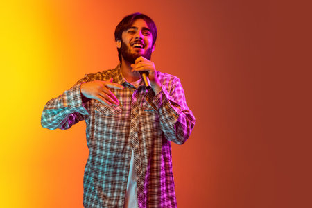 Cropped studio portrait of young boy singing in microphone, posing isolated over gradient yellow red...