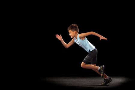 Full-length portrait of boy, athlete running, training isolated over black backgroundの写真素材