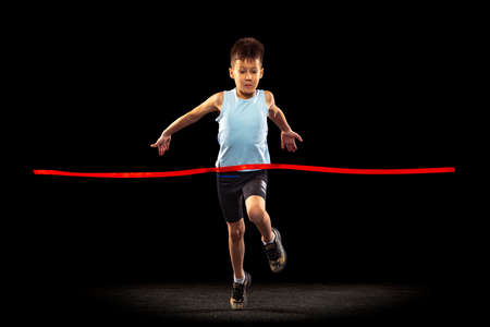 Full-length portrait of boy, child crossing red ribbon isolated over black background. Winnerの写真素材