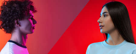 Collage. Portraits of young boy and girl looking at each other isolated over red background in neon lightsの写真素材