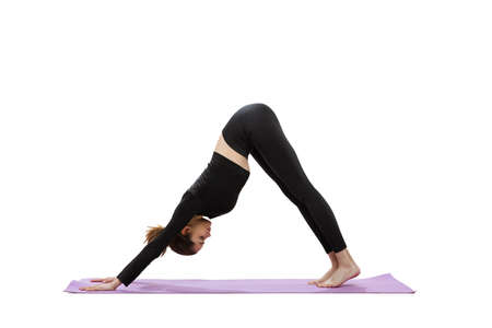 Portrait of young woman in black gym clothes training on purple yoga mat isolated over white studio...