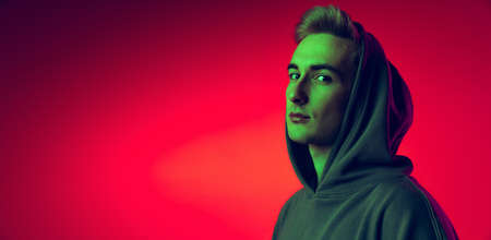 Portrait of young man in stylish hoodie with hood on head posing, looking at camera isolated over...