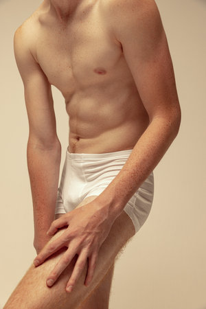 Cropped image of sportive male body in underwear, muscular shape, abs, hands. Model posing in underwear isolated on studio background. Concept of male beauty, fashion, mens health, wellness, fitnessの写真素材