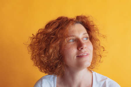 Portrait of beautiful woman with curly red-haired hair in white casual T-shirt posing isolated over...