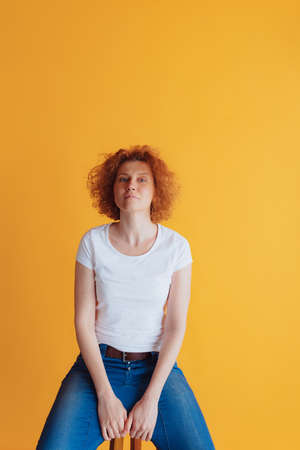 Portrait of beautiful woman with curly red-haired hair in white casual T-shirt sitting, posing...