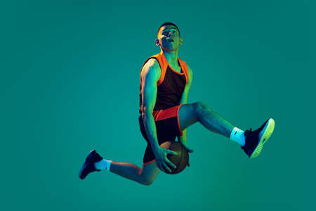 Portrait of young man, professional backetball player in motion, training isolated over blue background in neon light. Jump shot. Concept of sport, team game, action, active lifestyle, adの写真素材