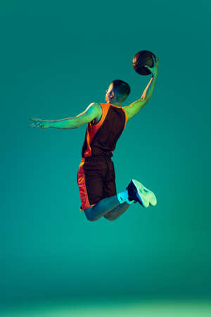Portrait of young man, professional backetball player in motion, training isolated on blue...