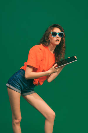 Portrait of young girl in casual outfit, shorts and T-shirt, holding tablet, posing isolated over...